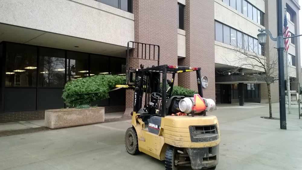 A large holiday wreath being carried by a small forklift